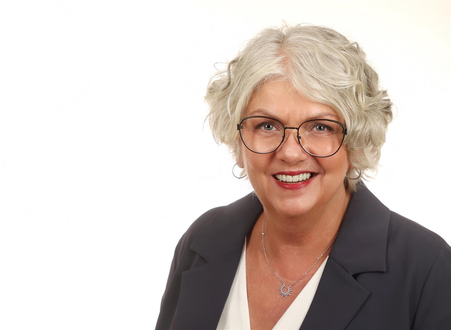 Das Porträtfoto einer Frau mit weißen Haaren udn Brille.